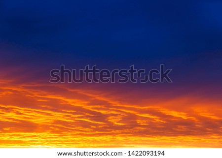 Colorful dramatic sky at sunset with layered rain clouds of bright blue and orange. A beautiful picture can be associated with the sea and lava.