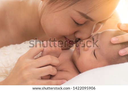 beautiful young  mother holding and kiss her newborn baby's cheek and her baby holding her finger  with love and care on white background bed