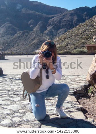 Mature woman takes pictures of kneeling to a landscape in Los Roques, next to the Teide in Tenerife, Canary Islands, Spain
