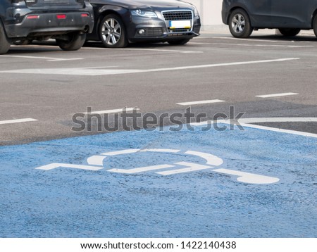 A special car parking space for disabled people. Easy wheelchair accessibility for the handicapped on the parking lot concept. Blue symbol / icon on the asphalt in the urban environment, closeup