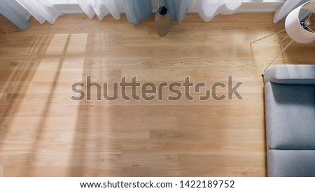Cozy Living Room with Modern Interior, Grey Sofa and Wooden Flooring Lit By Warm Light out of the Window. Top View Camera Shot. Royalty-Free Stock Photo #1422189752