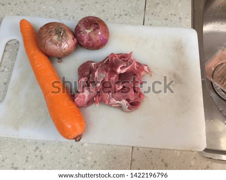 Cross contamination of food, raw beef meat on the same chopping board with onion and carrot
