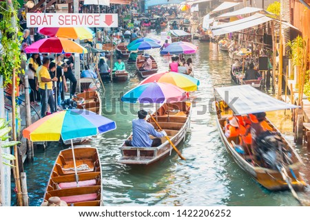 Damnoen Saduak Floating Market, tourists visiting by boat. The text on boats translate into English is coconut ice cream, mango and sticky rice, grilled chicken and pork. Located in Bangkok, Thailand. Royalty-Free Stock Photo #1422206252