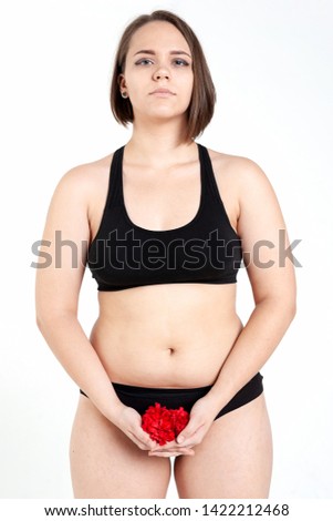 Body positive and feminism concept. Girl plus size model in black underwear holds red flowers at the level of the lower abdomen. The theme of women's health, reproductive health, menstruation.