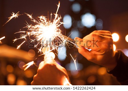Chain Reaction Bengal Lights. Bengal lights in male hands set fire to each other on Christmas tree lights background
