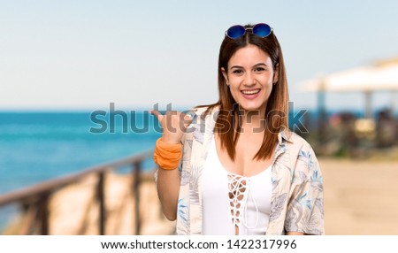 Young woman in bikini in summer holidays pointing to the side to present a product at the beach