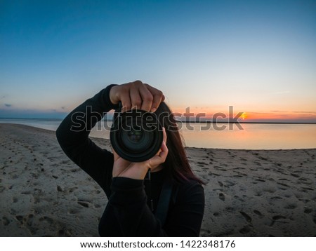 Girl with the camera taking pictures of the photographer at the sunset with the ocean and the beach behind