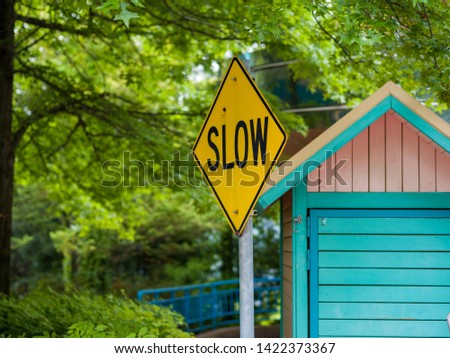 Yellow Slow Traffic Sign on the Roadside with Trees in the Background and Pastel Wooden Shack