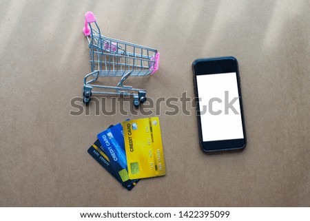 shopping cart, smartphone with credit card on brown background. soft focus.