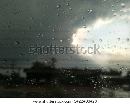 blur background rain drop on glass window with dark sky and sun light.