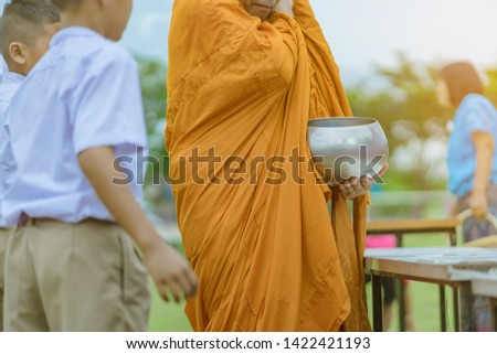 Teachers and students together make merit to give food offerings to a Buddhist monk on important religious days at school.