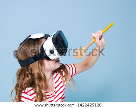 cool and smiling positive girl wearing virtual reality glasses goggles headset is singing with cooking spoon, new generation, concept in front of blue background