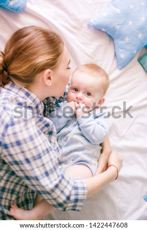 Portrait of beautiful mom in shirt and blue jeans playing with her  baby boy in bedroom
