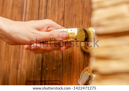 Female hand holding the golden handle of a wooden door close up