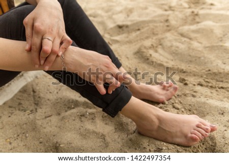 Young woman having rheumatoid arthritis takes a rest sitting on the sand near the beach. Hands and legs are deformed. She feels pain. Selected focus.