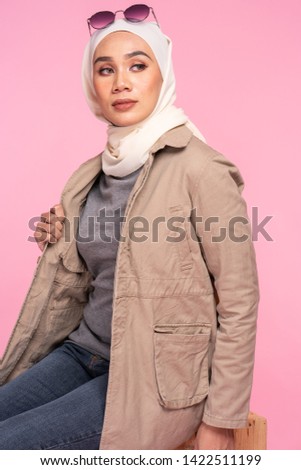 Fashionable young woman in jeans, long sleeves bush jacket and hijab isolated on pink background. Stylish Muslim female hijab fashion lifestyle portraiture concept.
