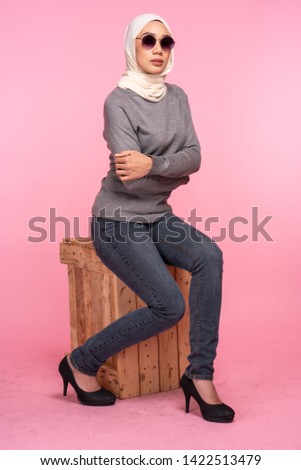 Fashionable young woman in jeans, long sleeves sweatshirt and hijab isolated on pink background. Studio fashion and beauty concept.