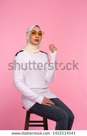 Fashionable young woman in jeans, long sleeves sweatshirt and hijab isolated on pink background. Studio fashion and beauty concept.