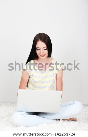Beautiful young woman sitting on carpet with laptop in room