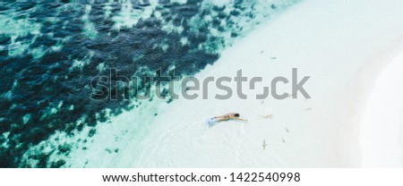 Woman snorkeling with many small sharks near white sand beach in turquoise clean water. Drone aerial view. Tropical background and travel concept