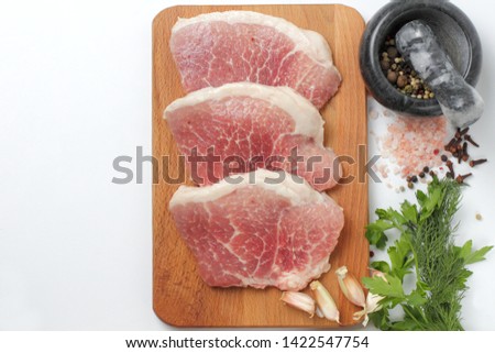 Large pieces of fresh pork on a cutting board, pink salt, cloves, allspice in a mortar, spicy herbs, top view, place for text, close-up on a white background.