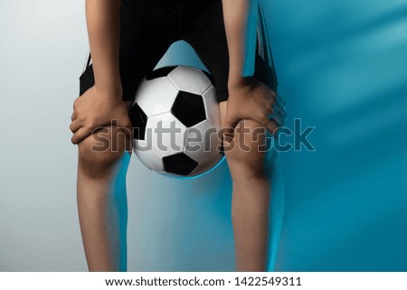 football goalkeeper with dirty knees clamped the ball between his legs on a blue background