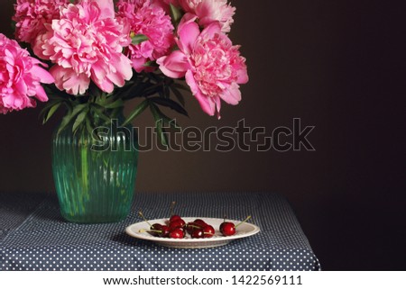 peonies and cherries. still life with a bouquet of flowers in a vase and a plate of berries. copy space.