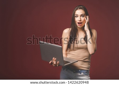 Happy beautiful girl in shirt using laptop. Excited woman with tablet pc, isolated on red background.