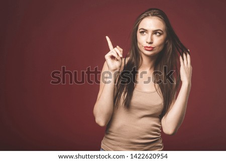 Photo of happy young woman standing isolated over red wall background. Showing copyspace pointing. 