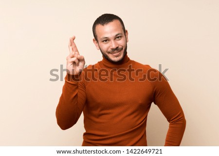 Colombian man with turtleneck sweater with fingers crossing and wishing the best