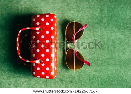 A red white polka-dot female glasses case and pink sunglasses on a green background imitating grass. Concept of summer and vacation