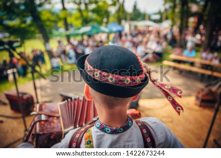 Young man playing on accordion in Slovak folk dress and folk hat. In front of the crowd