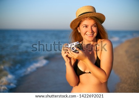 Young authentic woman with vintage retro film camera enjoying tropical beach on summer vacation. Female travel photographer in straw hat taking photos having fun at sea. Real girl unretouched shape.