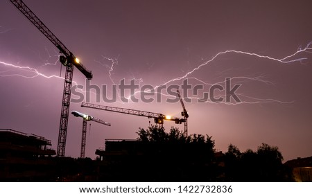 Lightning strikes behind the cranes of a construction site in a thunderstorm