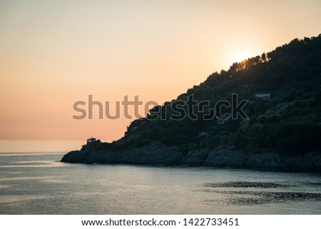 The view of mediterranean sea, small chapel on the rocks and beautiful golden sunset colour sky. La Madonnina della Punta, Bonassola, Liguria, Italy