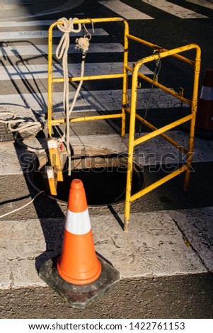 Street warning orange construction cone near manhole protected with yellow security fence