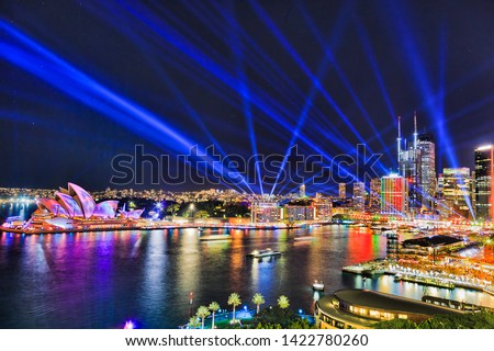 Sydney city CBD waterfront of Circular quay with high-rise buildings painted by light and blue laser beams in dark night sky during Vivid Sydney light show. Royalty-Free Stock Photo #1422780260