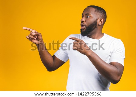 Afro american man over isolated background amazed while presenting with hand and pointing with finger.
