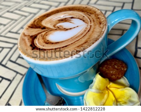 Cappuccino in blue cup with yellow flower and heart latte art. Shot in bali indonesia.