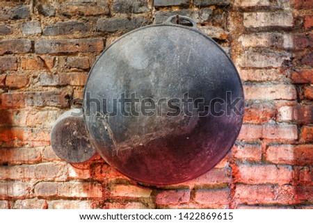 Close up black frying pan stick to the red brick wall. 