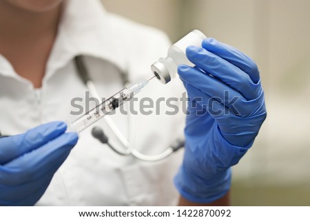Medication nurse wearing protective gloves and white scrubs get a needle or shot ready for an injection. Royalty-Free Stock Photo #1422870092