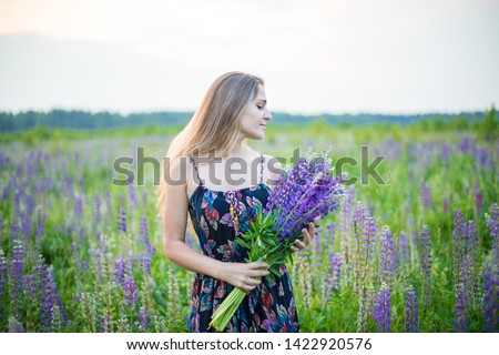 Young beautiful girl in a colorful dress with a bouquet of lupines in field