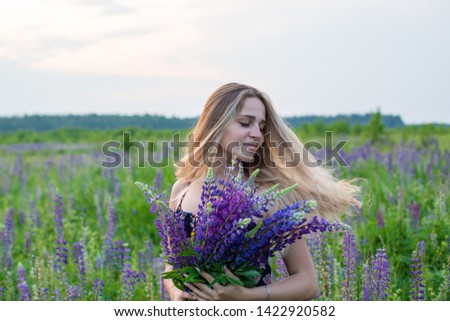 Young beautiful girl in a colorful dress with a bouquet of lupines in field