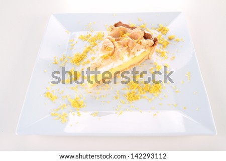 Slice of Lemon Meringue Tart on a plate decorated with lemon peel