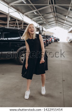 Stylish young girl dressed in a comfortable, daily black dress and white sneakers pose for a photo on an industrial background, urban clothing style. Street photography