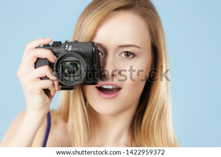 Photographer girl shooting images. Lovely blonde smiling woman with camera on blue background
