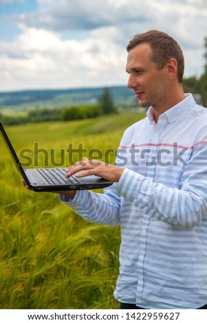 businessman with laptop and smartphone working in wheat field in blue sky background.