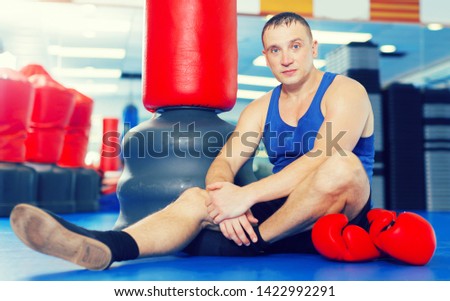 Young male boxer is sitting on the floor after training in gym