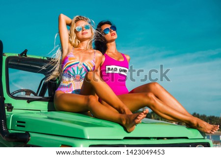 Two incredible beautiful young girls in bikini swimsuits, traveling around a tropical island in a cabriolet off-road car, summer vacation
