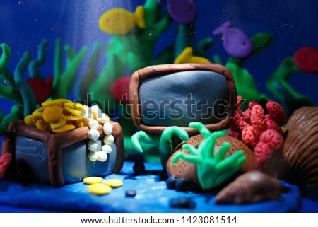 Plasticine underwater landscape. The ocean and the undersea world background, corals and open pirate chest with shinny gold. There is an empty plate for text.